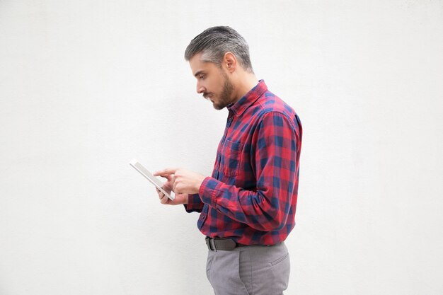 Homme barbu concentré à l'aide de tablette numérique