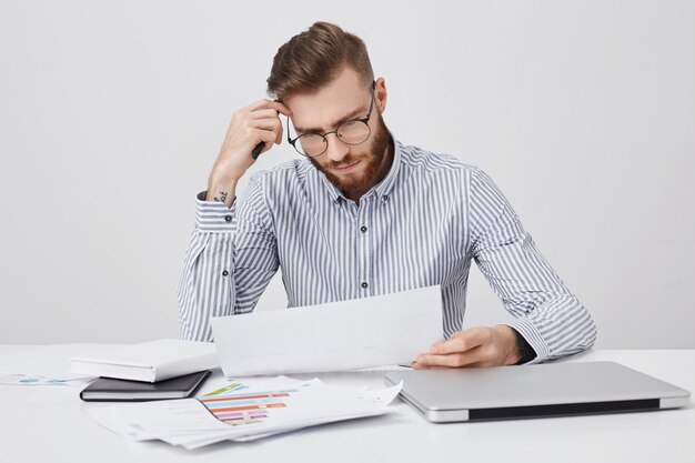 Homme barbu concentré sérieux habillé formellement, lit un document ou un contrat