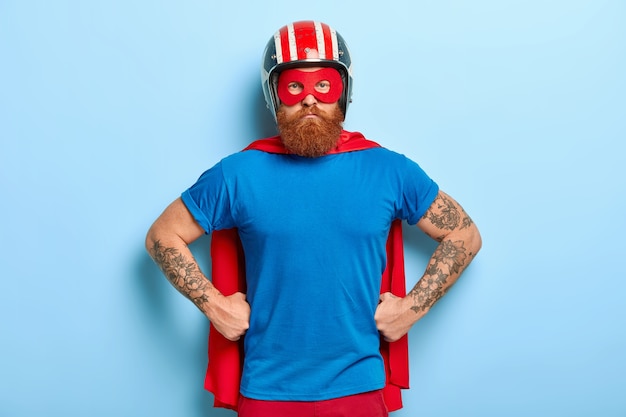 Un homme barbu confiant garde les mains sur la taille, prêt pour la défense, regarde avec un regard puissant et puissant directement sur la caméra, porte un casque