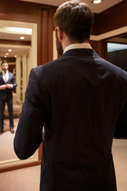 Homme barbu corrigeant son costume contre le miroir