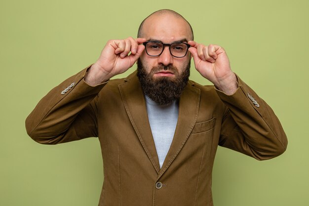 Homme barbu en costume marron portant des lunettes à toucher de près ses lunettes