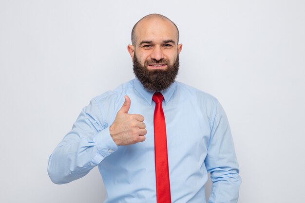 Homme barbu en cravate rouge et chemise bleue à sourire confiant montrant les pouces vers le haut