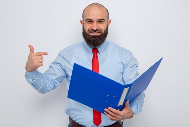 Homme barbu en cravate rouge et chemise bleue tenant un dossier de bureau à la recherche de l'article sur fond blanc