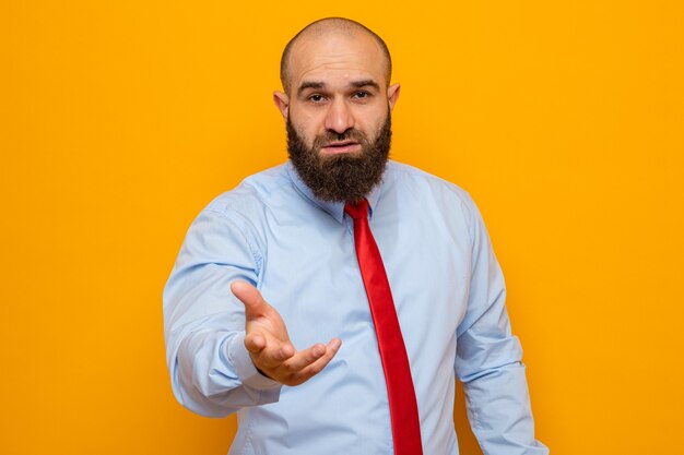 Homme barbu en cravate rouge et chemise à bras levant comme pour aller poser une question