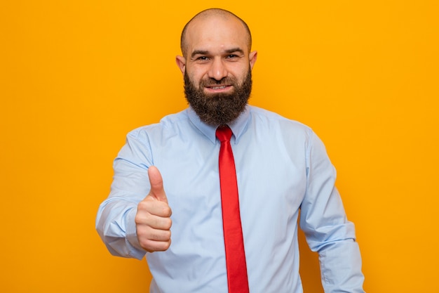 Homme barbu en cravate rouge et chemise à sourire confiant montrant le pouce vers le haut