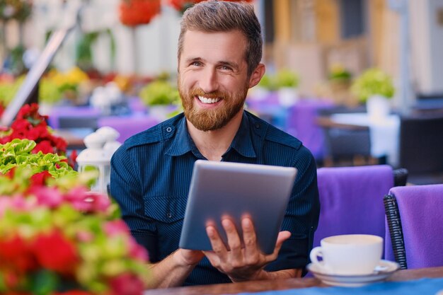 Un homme barbu décontracté boit du café et utilise une tablette PC dans un café.