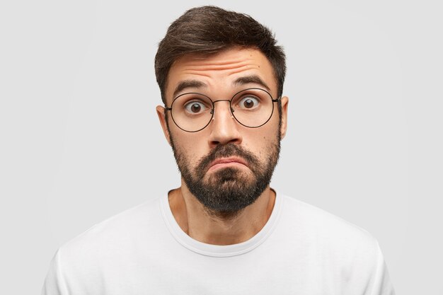 Un homme barbu douteux serre les lèvres avec hésitation, regarde la caméra avec une expression effrayée,