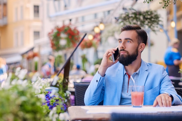 Photo gratuite homme barbu élégant dans une veste bleue parle par téléphone intelligent dans un café.