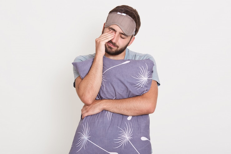 Photo gratuit homme barbu endormi posant avec les yeux fermés isolé sur mur blanc, se frottant les yeux avec la main, embrassant l'oreiller