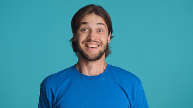 Homme barbu excité à la surprise de l'appareil photo sur fond bleu Beau mec ayant les yeux pleins de bonheur