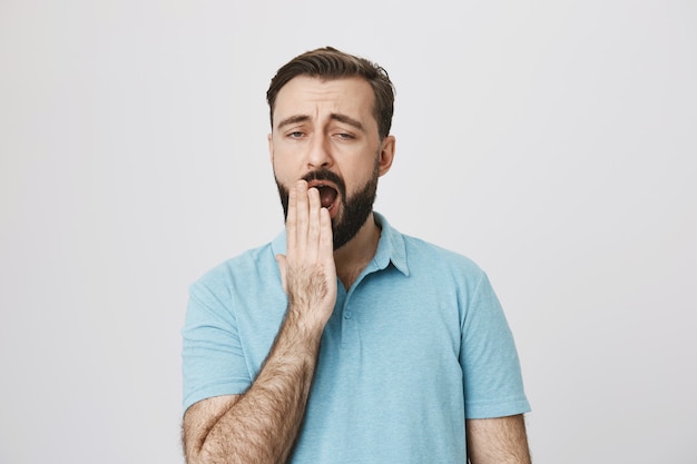 Homme barbu fatigué ou ennuyé bâillant, l'air réticent