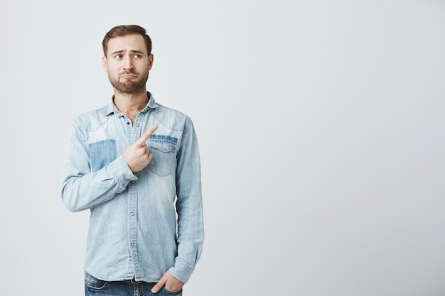 Homme barbu fronçant les sourcils sceptique pointant et regardant le coin supérieur droit