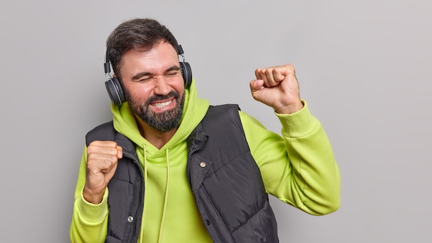 L'homme barbu insouciant s'amuse aime la musique préférée fait oui le geste garde les bras levés danse