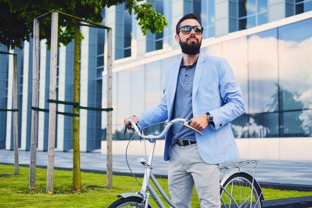 Homme barbu de luxe dans des lunettes de soleil sur un vélo dans un centre-ville.