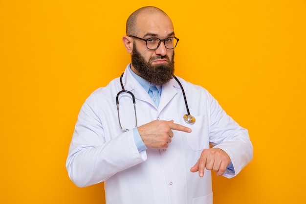 Homme barbu médecin en blouse blanche avec stéthoscope autour du cou portant des lunettes regardant pointant avec le doigt atm sa main rappelant le temps