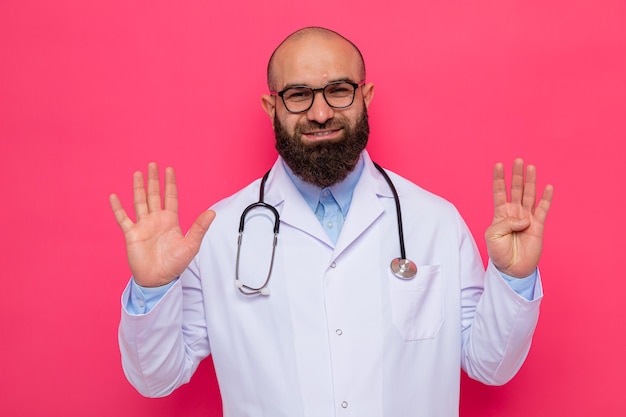 Homme barbu médecin en blouse blanche avec stéthoscope autour du cou portant des lunettes à sourire montrant le numéro neuf avec les doigts