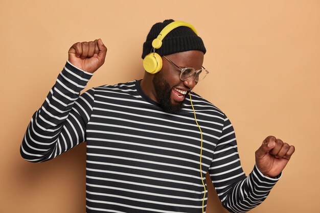 Un homme barbu noir ravi se déplace au rythme de la musique, porte des lunettes transparentes
