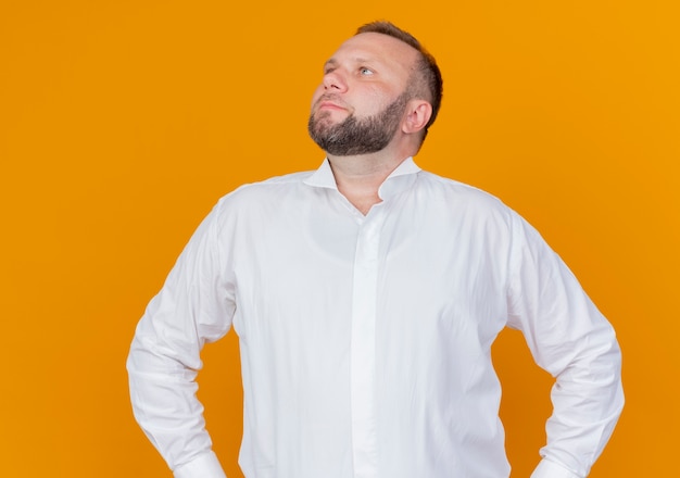 Homme barbu portant une chemise blanche à côté avec une expression sérieuse debout sur un mur orange