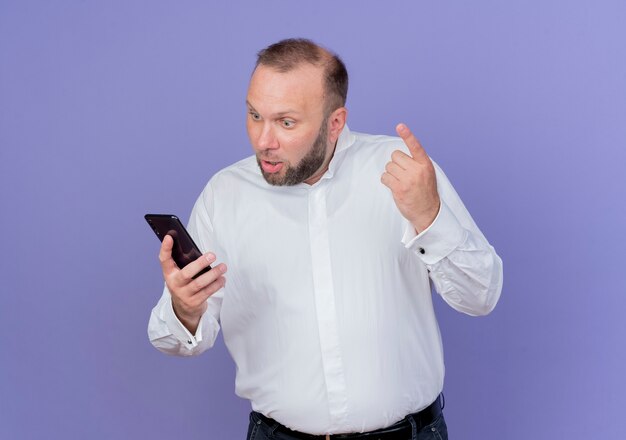 Homme barbu portant une chemise blanche debout sur un mur bleu