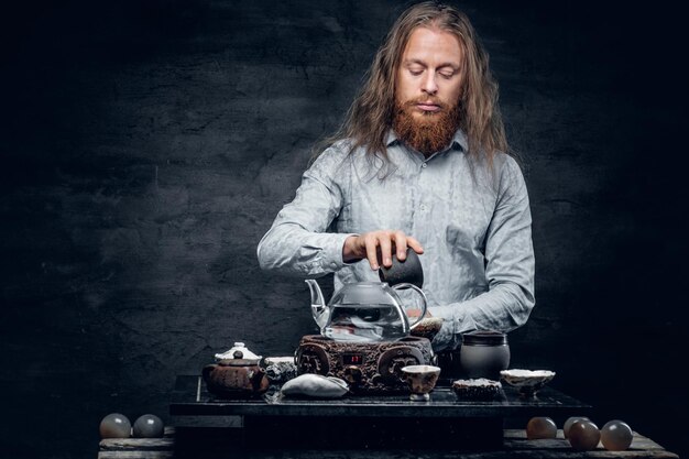 Un homme barbu positif verse de l'eau chaude lors d'une cérémonie du thé.