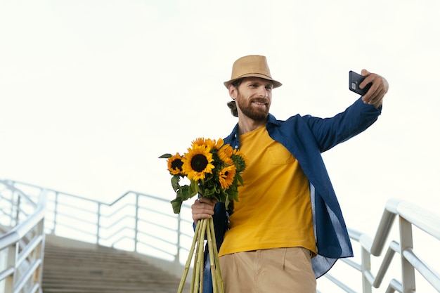 Photo gratuite homme barbu prenant selfie avec bouquet de tournesols