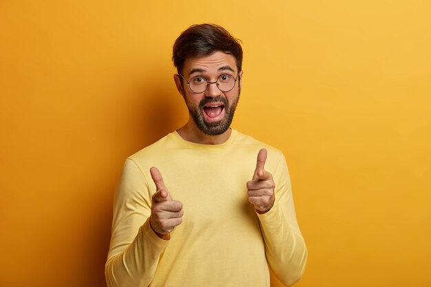 Un homme barbu ravi positif qui fait appel à vous, montre du doigt, fait le bon choix, a une drôle d'expression joyeuse, choisit quelqu'un, vous montre son geste, choisit un client potentiel