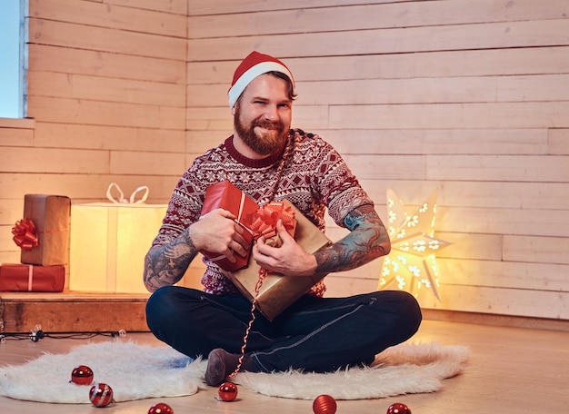 Homme barbu rousse en bonnet de Noel dans une chambre avec décoration de Noël.