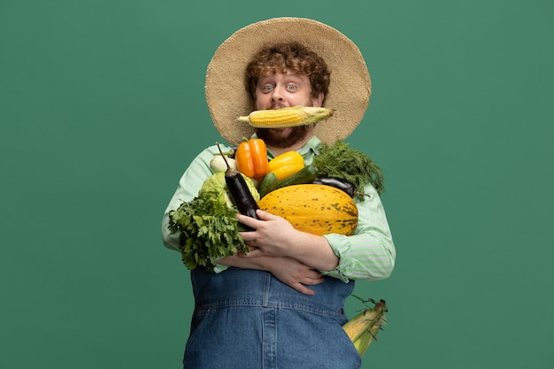 Photo gratuite homme barbu roux, agriculteur avec récolte de légumes isolé sur le mur vert du studio.