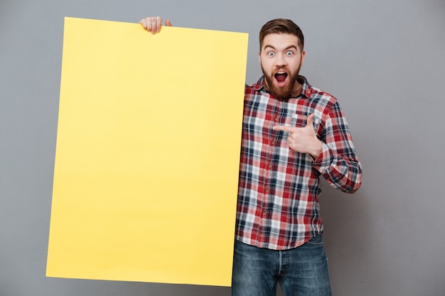 Homme barbu séduisant tenant un tableau blanc et pointant