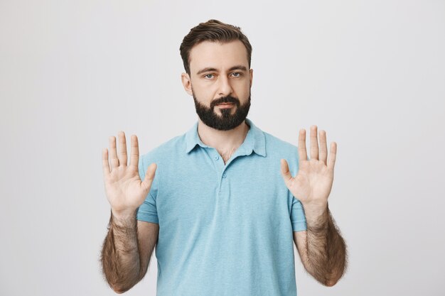 Homme barbu sérieux montrant le geste d'arrêt, les mains vides