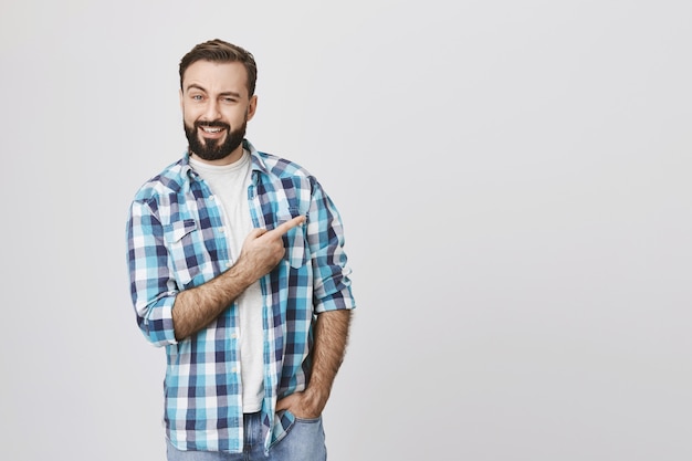 Homme barbu souriant intrigué pointant le doigt dans le coin supérieur droit