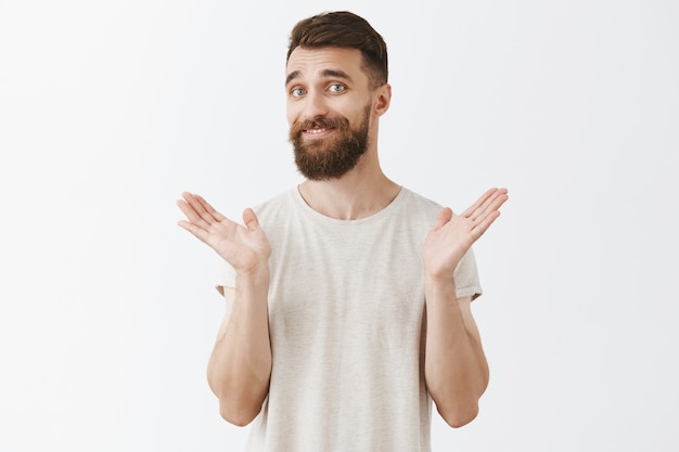 Homme barbu souriant réticent posant contre le mur blanc