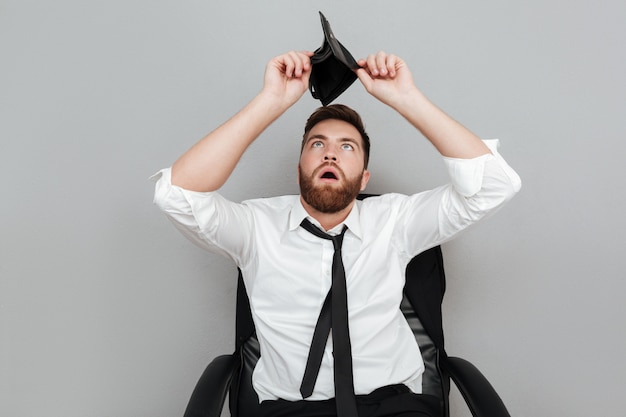 Photo gratuite homme barbu surpris frustré en chemise blanche montrant un portefeuille vide