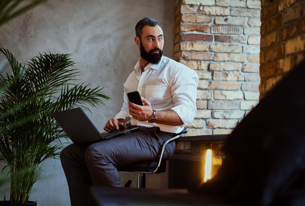 Homme barbu urbain utilisant un ordinateur portable dans une chambre avec intérieur loft.