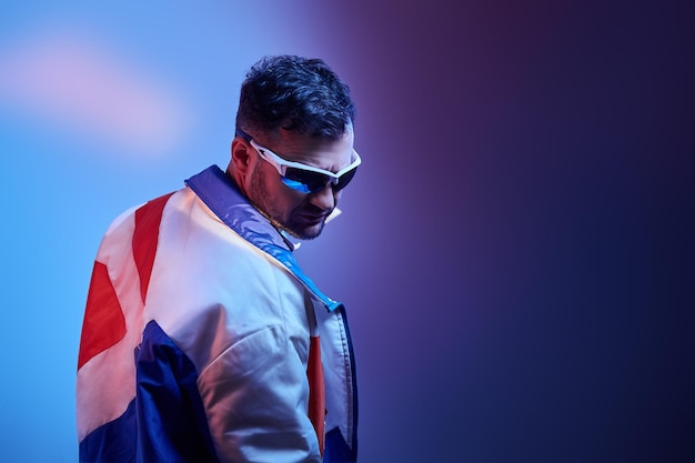 Un homme barbu en veste élégante pose pour le photographe dans des lumières bleues et rouges.