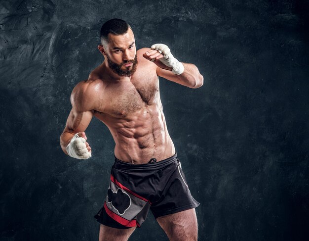 Homme barbu viril avec un beau torse musclé pose pour le photographe sur le fond sombre.