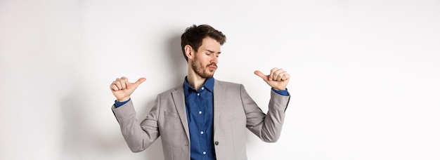 Homme beau et confiant en costume pointant vers lui-même se sentant cool et impertinent autopromouvant son bien