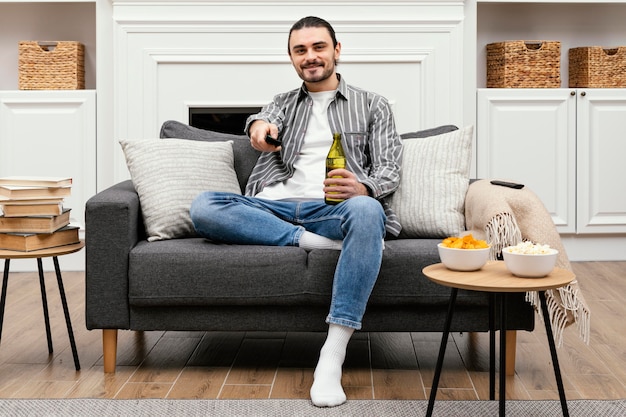 Homme bénéficiant d'une bière et regarder la télévision assis sur le canapé