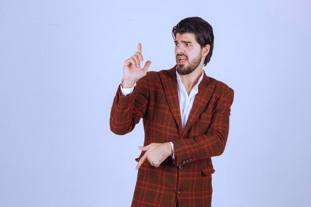 Homme en blazer à carreaux ayant un discours dans la scène et présentant quelque chose ci-dessus.