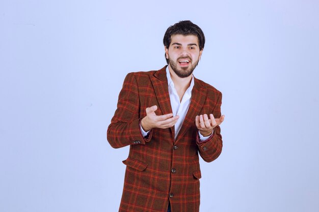 Homme en blazer à carreaux ayant un discours dans la scène et présentant quelque chose ci-dessus.