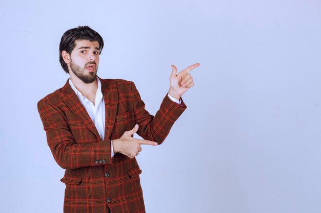 Homme en blazer à carreaux montrant quelque chose à droite et en parlant.