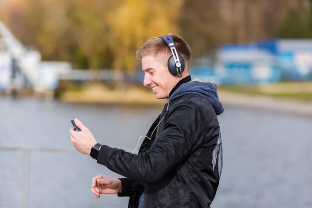 Photo gratuite homme blond souriant sur le côté, écouter de la musique à l'extérieur