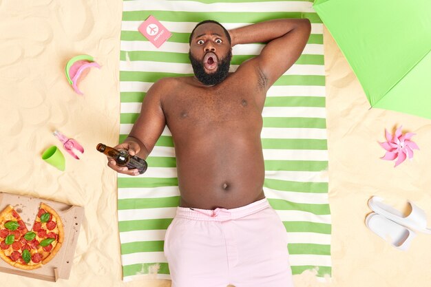 l'homme boit de la bière garde la bouche ouverte et regarde étonnamment bronzer à la plage passe des vacances d'été dans un lieu de villégiature profite du temps libre réagit aux nouvelles choquantes