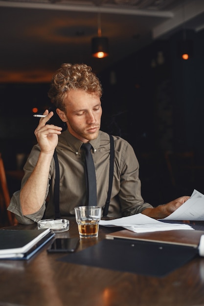 L'homme boit du whisky. Homme d'affaires lit des documents. Réalisateur en chemise et bretelles.