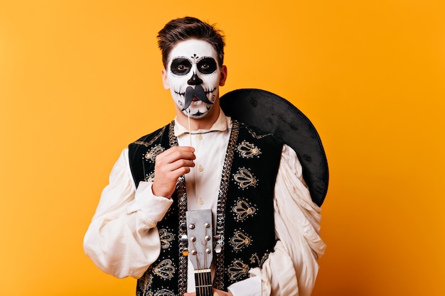 Homme de bonne humeur en costume de mascarade debout sur un mur jaune. Mec latin en sombrero célébrant l'halloween.