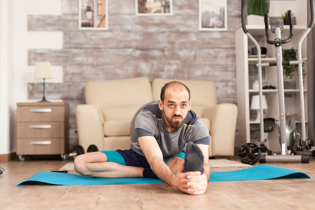 Homme en bonne santé faisant des exercices de mobilité sur un tapis de yoga à la maison pendant la pandémie mondiale.