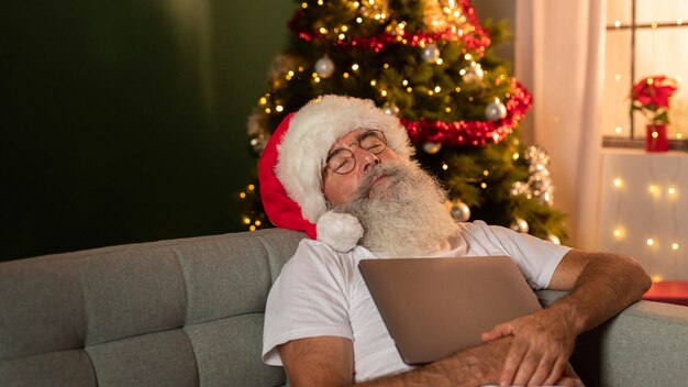 Homme en bonnet de Noel dormir à la maison tout en tenant son ordinateur portable