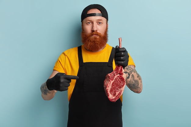 Homme boucher avec barbe au gingembre tenant de la viande