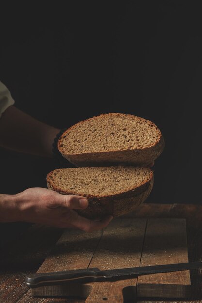 L'homme boulanger tient dans ses mains des moitiés de pain de seigle sur le fond de l'ancienne table brune