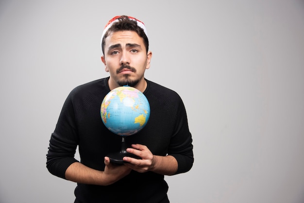 Homme bouleversé au chapeau du père Noël posant avec un globe.